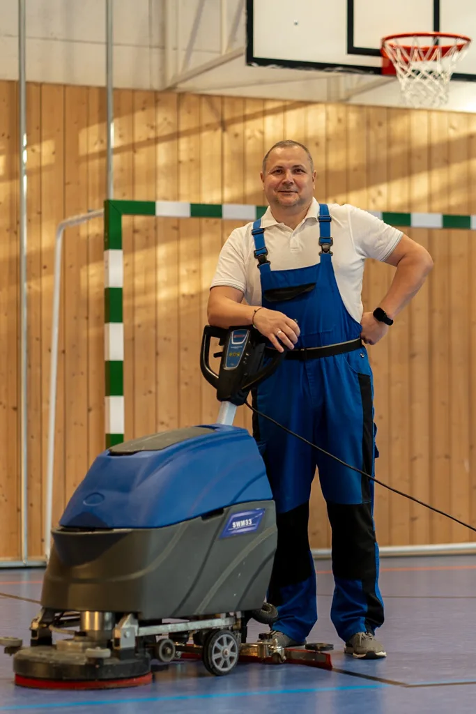 Mitarbeiter mit Bodenreinigungsmaschine in einer Sporthalle